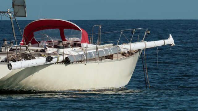 Sailboat moored in clear blue water with a red bimini top and stowed mast, symbolizing leisure, vacation, and ocean travel