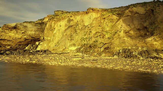 eroding cliffs at golden hour, visual warning of shoreline retreat and rising tides, textured rock face and wet sand underscore climate risk and urgent