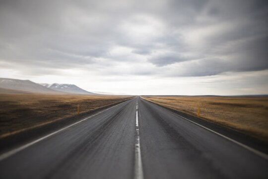 Panoramic view of an empty asphalt road extending into the distance under cloudy skies.