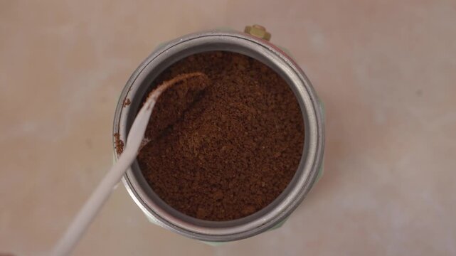 Adding ground coffee into italian moka pot filter basket before brewing traditional homemade coffee from top view.