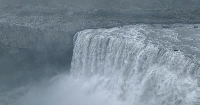 Dettifoss waterfall thundering along Jokulsa Fjollum River in Vatnajokull National Park, Northeast Region, Iceland, generating dense spray above basalt cliffs and volcanic bedrock, drone slow motion