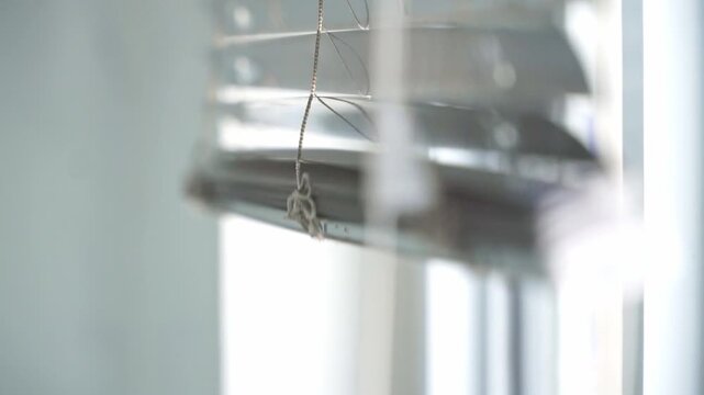 Hand releasing a blind cord to decreasing daylight inside a room. Residential interior scene emphasizing natural lighting and privacy management.