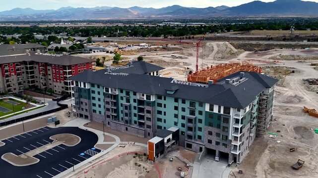 Completed apartment building with parking area, entrance, active wood-frame construction and earthworks in Taylorsville, Salt Lake County, Utah, Salt Lake Valley, Wasatch Range, drone parallax.