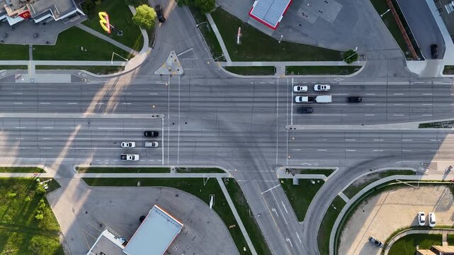 Drone aerial over busy Winnipeg intersection, Manitoba, Canada. Camera slowly descends toward road showing cars, streetlights, sidewalks, grass and surrounding buildings.
