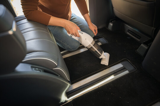close up hand of woman using portable handheld vacuum cleaner to cleaning the floor mat of her luxury car