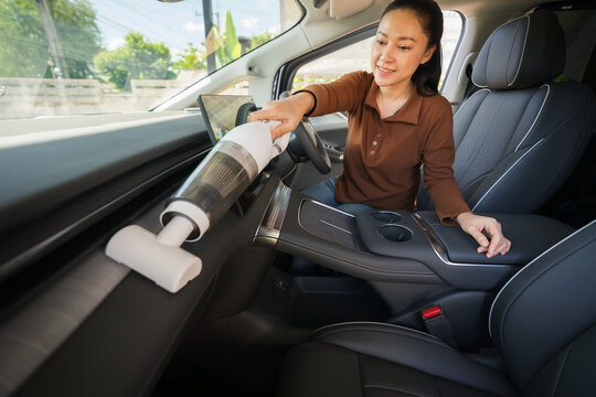 woman using portable handheld vacuum cleaner to clean dust on an electric car dashboard