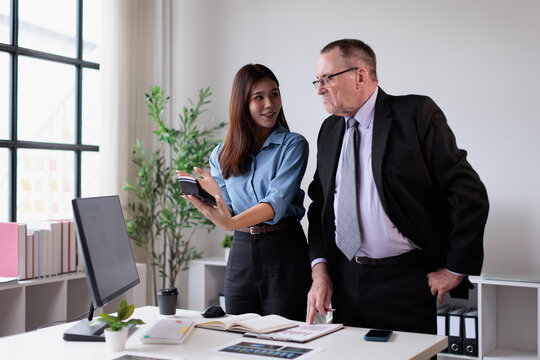 Young asian businesswoman actively collaborating and discussing financial data with a senior caucasian male colleague during a standing meeting in a bright corporate office