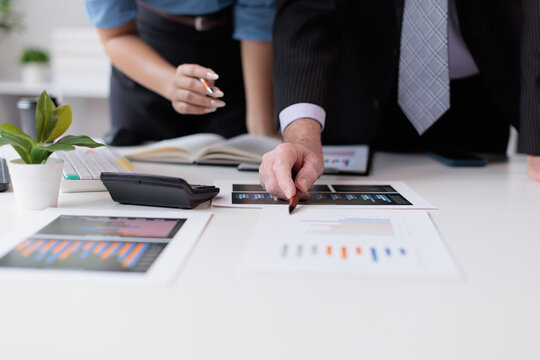 Business professionals analyzing financial data and statistics on documents, collaborating on market reports and corporate strategy in an office environment