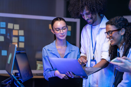 Wide shot of a diverse, multiethnic software team hand documents around while standing in a modern technology office bathed in blue light, highlighting diversity and teamwork in (frame 930)