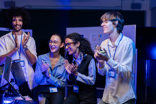 Low-light scene where a diverse, multiethnic software team applaud and cheer together against a deep-blue studio backdrop, a portrait of inclusion and collaboration in modern tech