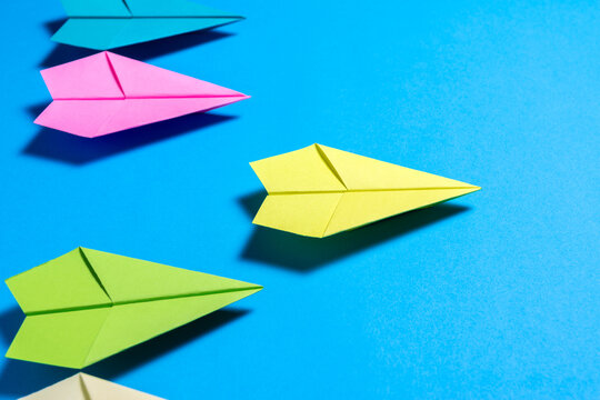 Yellow Paper Airplane Flying Ahead of Others on Blue Background