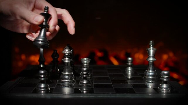 A hand moving a silver chess king piece on a board with dramatic orange lighting and other pieces visible in the scene.