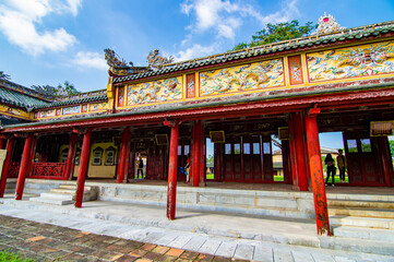 Obraz premium The red royal corridor inside the Imperial Citadel of Hue, Vietnam, featuring ornate gold carvings, traditional wooden pillars, and hanging lanterns under a UNESCO World Heritage site.
