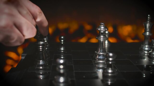 A hand knocking over or moving a silver chess piece on a board with dramatic orange lighting and scattered pieces visible.