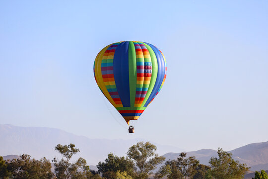 A hot air balloon flying on the sky with view of trees and mountains.