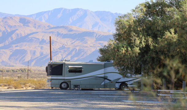 A large RV at an RV park under a shaded area by a picnic table.