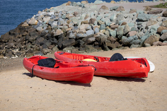 Two Red Kayaks on Sandy Beach Near Rocky Coastline