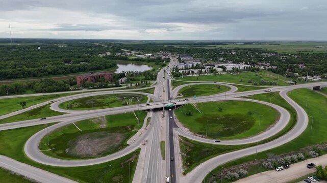 Drone static high above the Pembina Highway and Perimeter Highway cloverleaf interchange in Winnipeg looking south toward St. Norbert with traffic, Red River, green grass and partly cloudy summer.