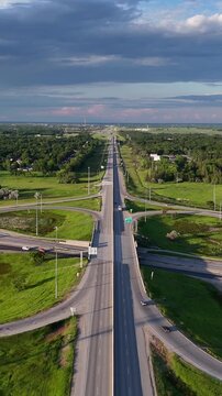 Vertical drone aerial of the Perimeter Highway cloverleaf interchange in St. Norbert, Winnipeg, Manitoba, Canada. Camera slowly backs up east along highway showing traffic, Red River, grass, buildings