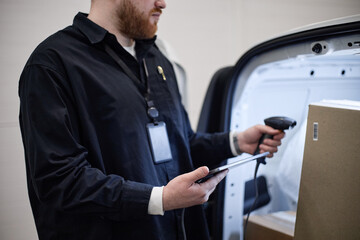 Fototapeta premium Caucasian young adult delivery worker scanning package barcode with handheld reader and checking tablet at van, managing individual storage logistics. For shipping, inventory, fulfillment marketing