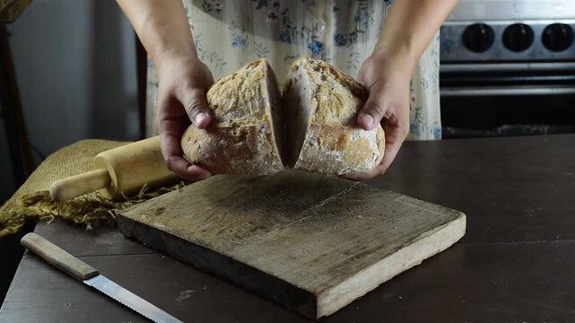 Close up shot of human hands slicing freshly baked sourdough bread on a rustic wooden cutting board in a cozy home kitchen. This is a professional homemade baking concept for healthy food.