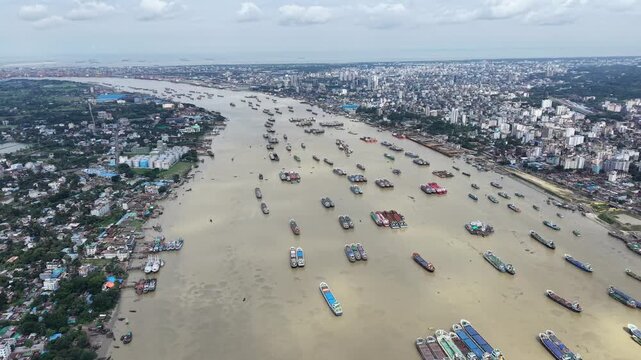 An aerial drone view showcases numerous cargo-carrying lighter vessels waiting out a local cautionary signal upstream on the Karnaphuli River in Chattogram, Bangladesh. 