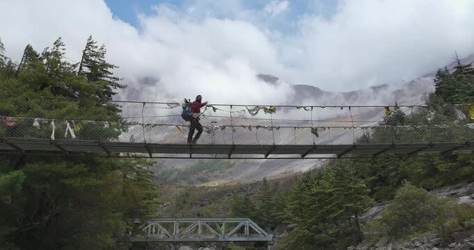 Annapurna Circuit, Manang region Nepal, aerial tilt-up shot revealing a suspension bridge over the Marsyangdi River over the vast pine forests and towering mountain landscape