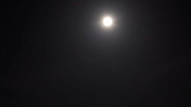 This video captures a bright full moon shining against a clear night sky.