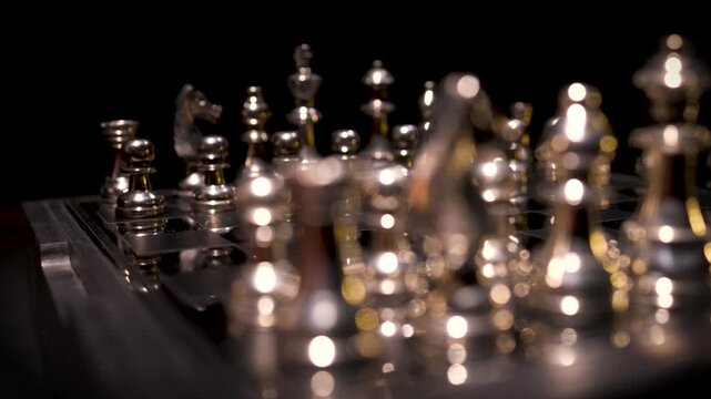 Silver chess pieces densely arranged on a dark board with dramatic lighting creating a complex mid-game position.