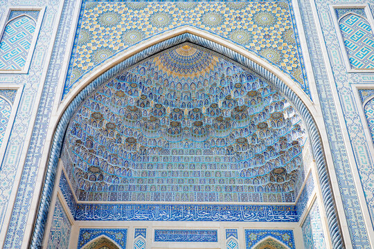 A breathtaking close-up of an ornate Islamic iwan featuring spectacular muqarnas vaulting, intricate blue mosaic tilework, elegant Arabic calligraphy, and mesmerizing geometric patterns
