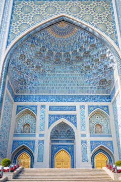 A breathtaking frontal view of a magnificent Islamic mosque entrance featuring elaborate muqarnas vaulting, intricate blue mosaic tilework, Arabic calligraphy, and elegant golden doors