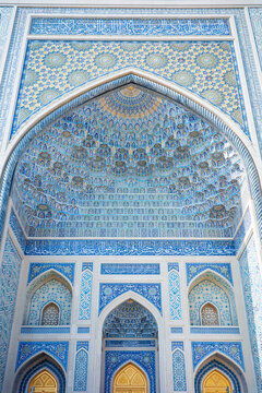 A magnificent frontal view of an Islamic mosque showcasing an elaborate muqarnas vault, intricate blue mosaic tilework, elegant Arabic calligraphy, and beautifully crafted golden doors
