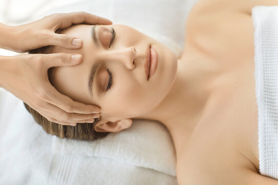 View from above of relaxed young woman enjoying facial massage from professional beautician in beauty clinic, taking care of her complexion and skin condition, lying relaxed with closed eyes