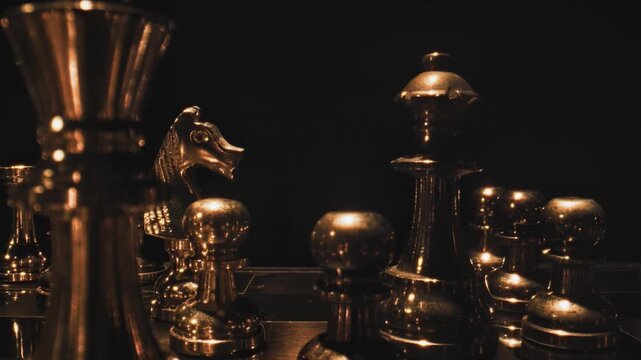 Dark chess pieces on a reflective surface with selective dramatic lighting and a predominantly dark moody background.