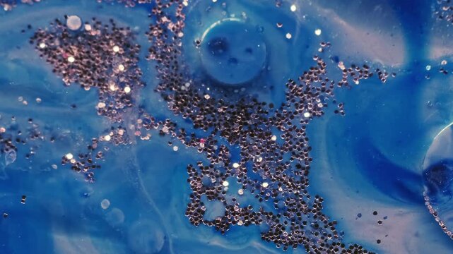 Shiny fluid texture. Shimmering art. Defocused blue color sequin bright particles floating in paint water wave on abstract background.