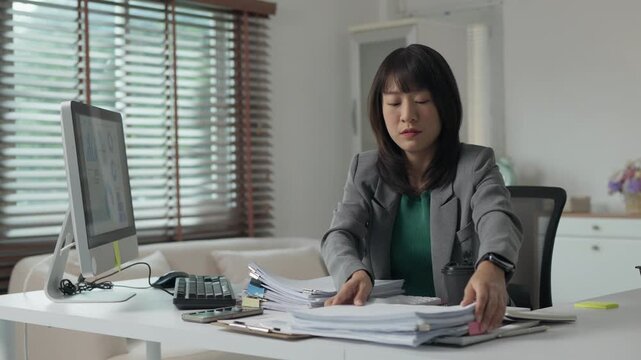 Stressed asian businesswoman managing paperwork at her office desk