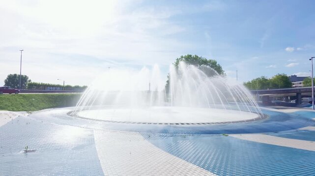 Expansive view of a vibrant circular fountain in Arnhem, Gelderland, Netherlands, with numerous water jets creating a dramatic display under a bright blue sky. Climate solution during heat wave.