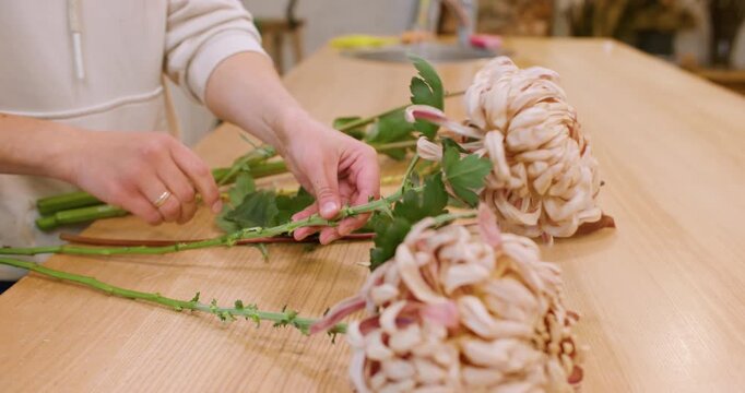 Flowers preparing. Floristry workshop. Unrecognizable floral designer working with seasonal green leaves autumn bouquet at wooden table.