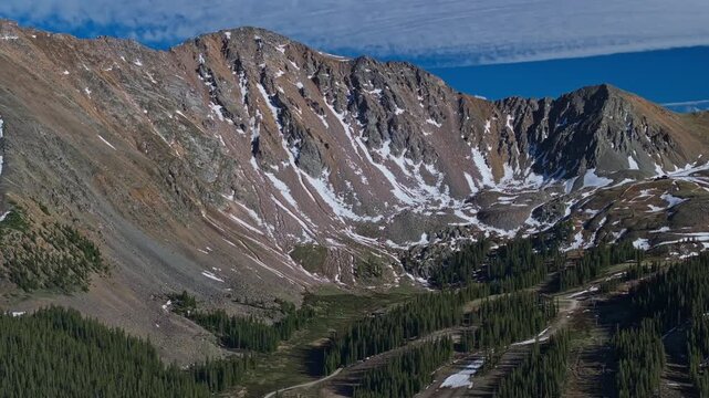 Steep alpine cirque with lingering snow below rocky summits, drone establishing tracking right of pristine exploration area