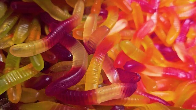 Macro close-up of colorful gummy worms piled together, with translucent candy texture, red, orange, yellow, and green colors, soft glow, and sweet shop display for candy retail footage.