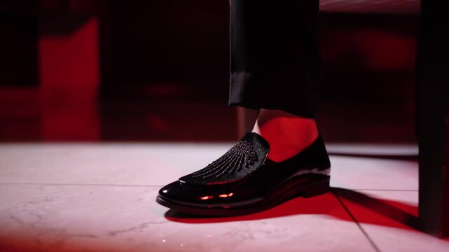 Close up of a man's feet wearing elegant black patent leather loafers with shiny rhinestones dancing at a party