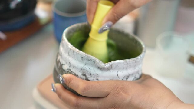 4K Close up of hand using traditional whisk to mix green matcha tea powder in clear glass bowl, Concept of traditional Japanese tea ceremony preparation and healthy lifestyle.
