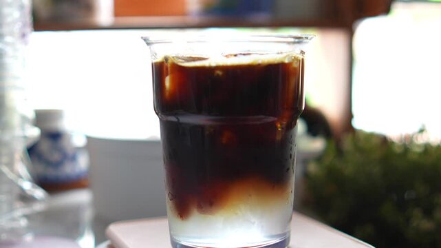 4K Close-up barista pouring hot espresso shot into plastic glass filled with ice and coconut water, Cafe beverage menus coffee shop marketing.