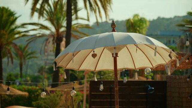White balinese-style sunshade offering relaxation and comfort in a tropical beach environment with palm trees and string lights