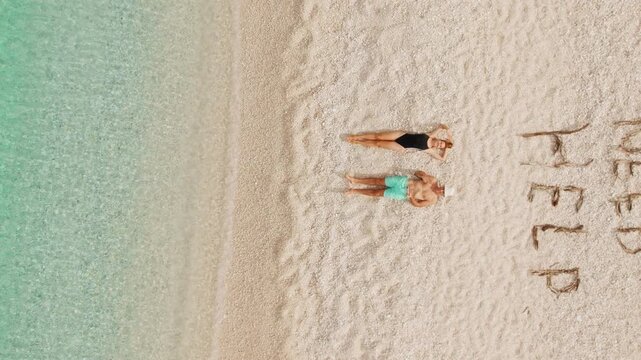 Couple relaxing on remote pebble beach beside clear turquoise sea with written words on shore WE DON'T NEED HELP