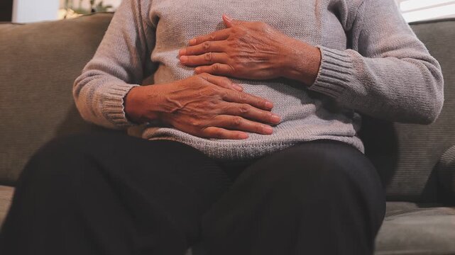 Stomach ache, cramps and hands of woman with abdomen pain due to constipation, menstruation or ibs issue. Sick, home and person suffering and holding belly in a house lounge, couch and living room