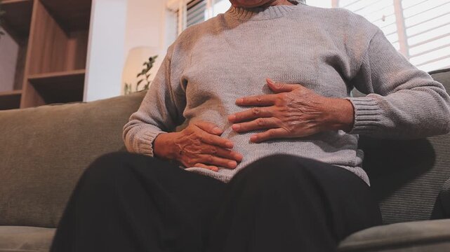 Stomach ache, cramps and hands of woman with abdomen pain due to constipation, menstruation or ibs issue. Sick, home and person suffering and holding belly in a house lounge, couch and living room