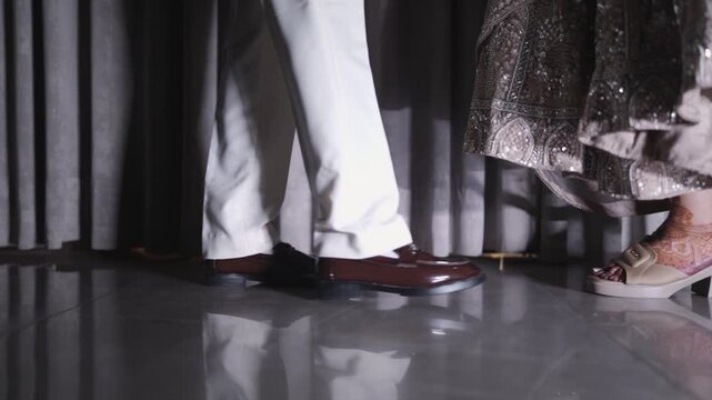 Low angle shot of an Indian bride and groom's feet showing traditional wedding footwear and lehenga details