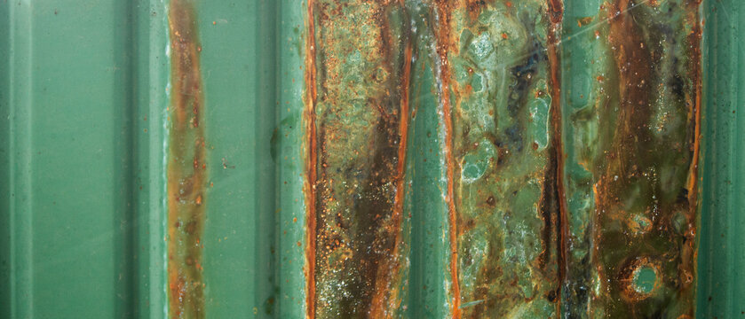 Close-up of rust texture on a green corrugated metal sheet.  A detailed close-up shot capturing the heavy rust and corrosion on a vibrant green corrugated metal wall or zinc sheet. 