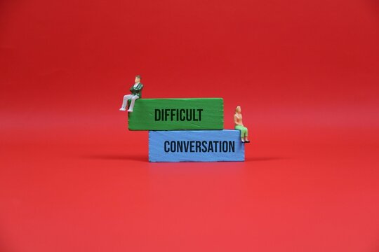 Difficult Conversation Concept With Miniature Couple Sitting on Stacked Blocks Against red Background. illustrating relationship conflict and the need for dialogue or counseling.